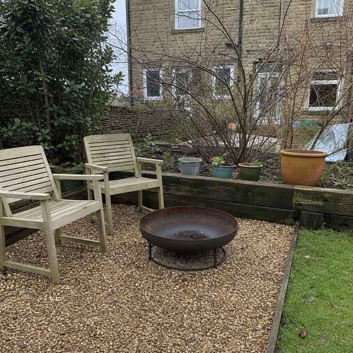 a simple metal fire pit on a level gravel base, unlit, daytime