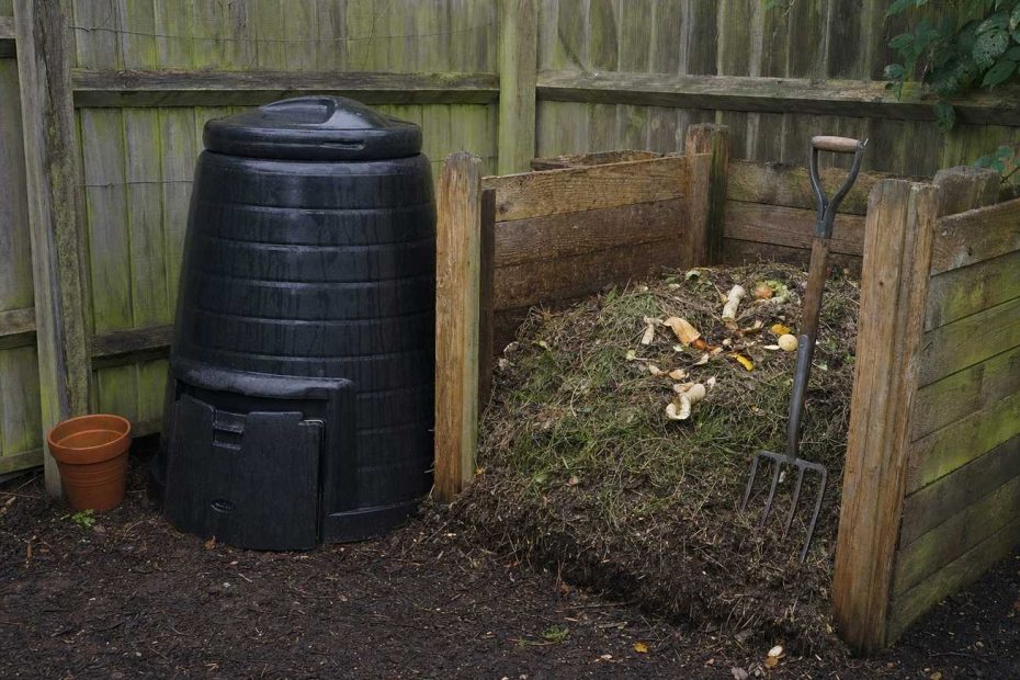 a dalek compost bin and open wooden heap in the corner of a garden